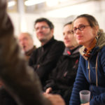 des gens assis regardent une personne hors champs dont on apperçoit le bras