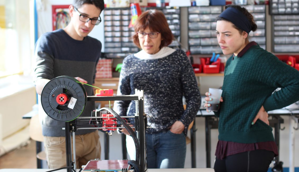 Troisperosnnes devant une imprimante 3D dans un atelier