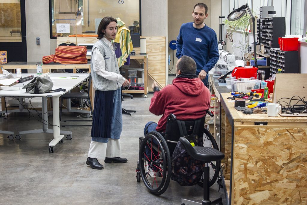 Photo de trois personnes en train de discuter dans un fablab. Au premier plan l'un d'eux est un homme en fauteuil roulant